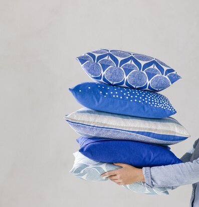 Kuddfodral Happy Kobolt från Spira i en hög med andra kuddar