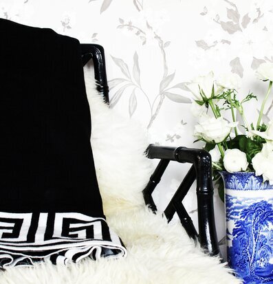 Pläd Santorini Svart från ELCE Stockholm på en svart stol