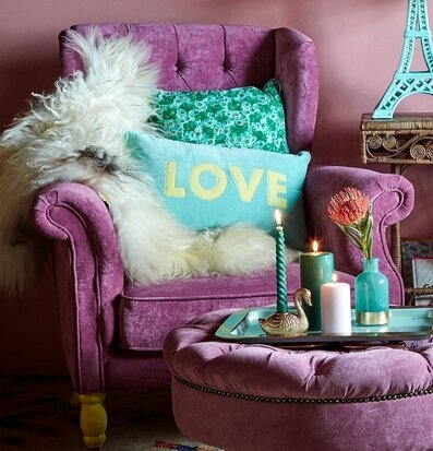 Sammetskudde Mintblå LOVE från Rice i lila fåtölj med fårskinn