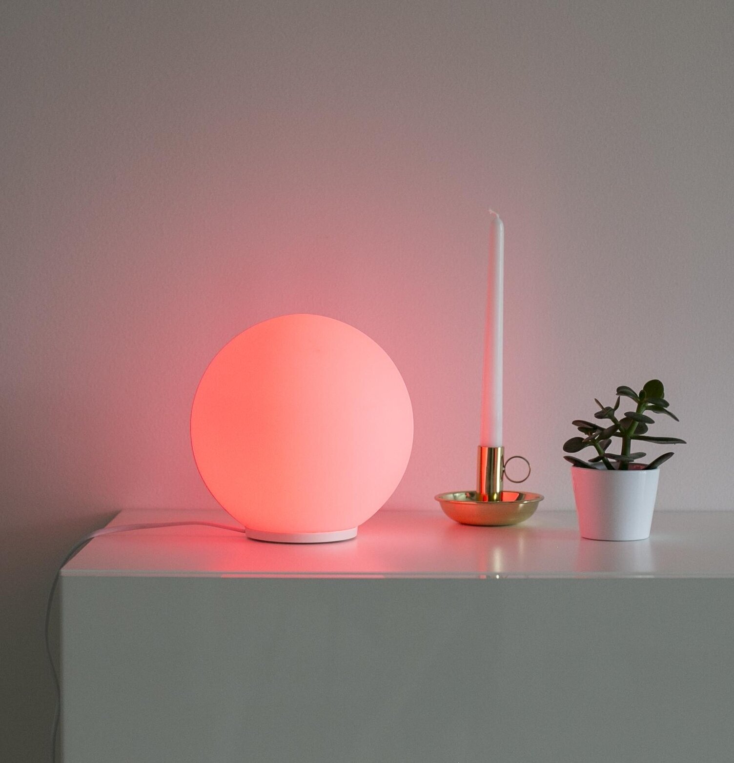 Glaslampa Rund från Havsö på vit yta med växt och ljus