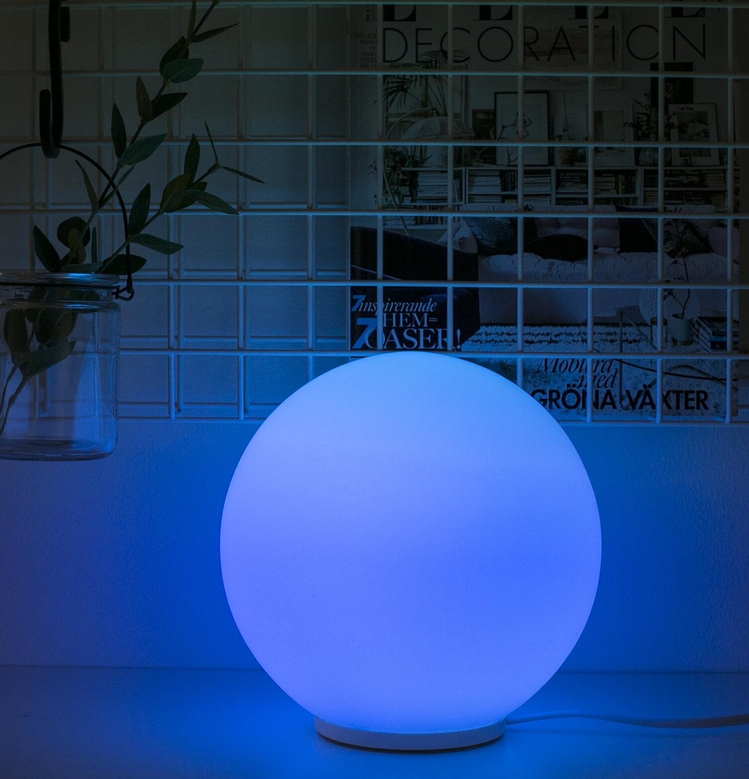 Glaslampa Rund från Havsö med blått sken på vit hylla