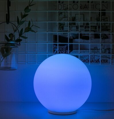 Glaslampa Rund från Havsö med blått sken på vit hylla