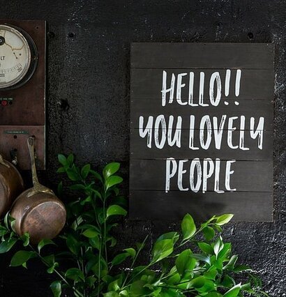 Tavla Hello - Majas Cottage på mörk vägg med grön växt