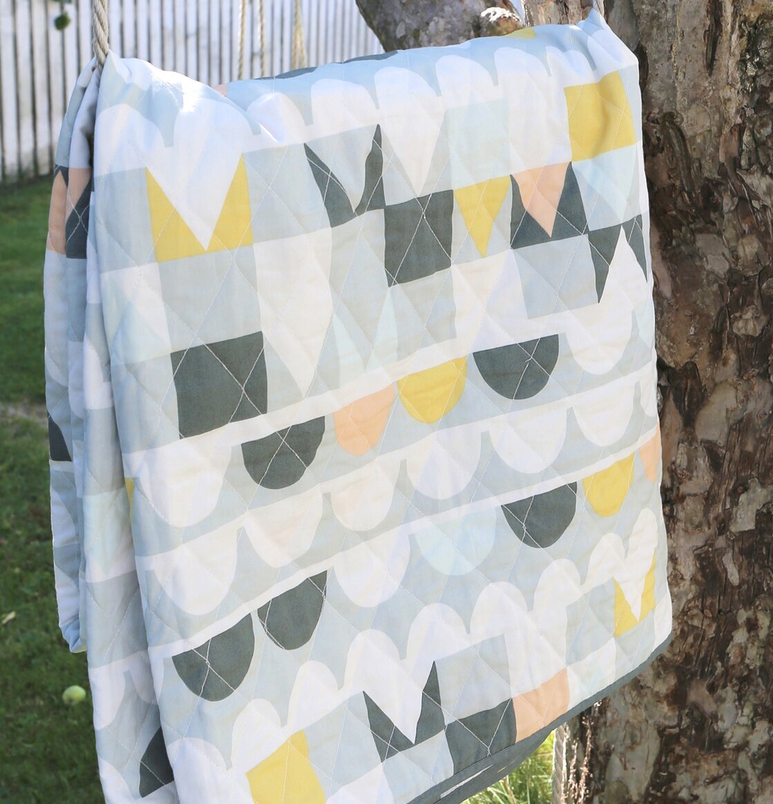 Quiltad Filt Tivoli Grå från Majvillan hänger i ett träd