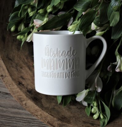 Mugg Mamma Vit från Majas Cottage omgiven av gröna blad