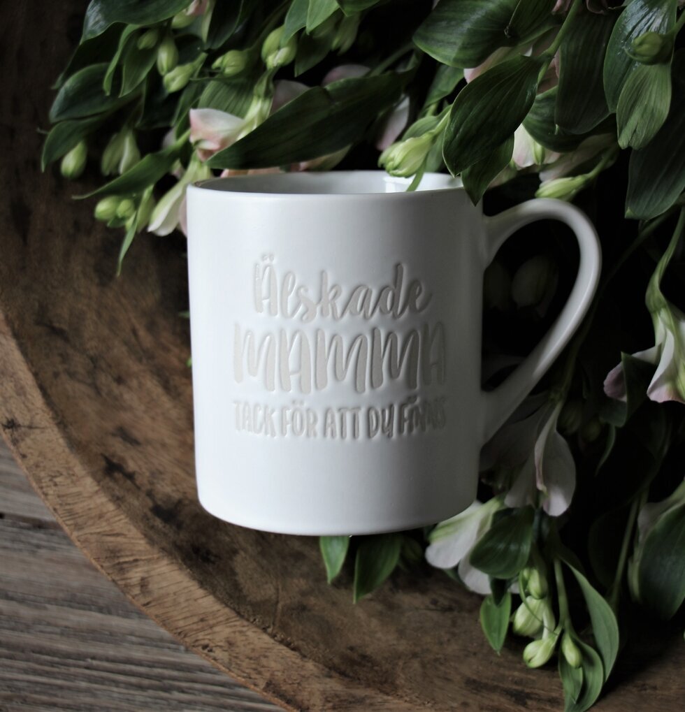 Mugg Mamma Vit från Majas Cottage omgiven av gröna blad