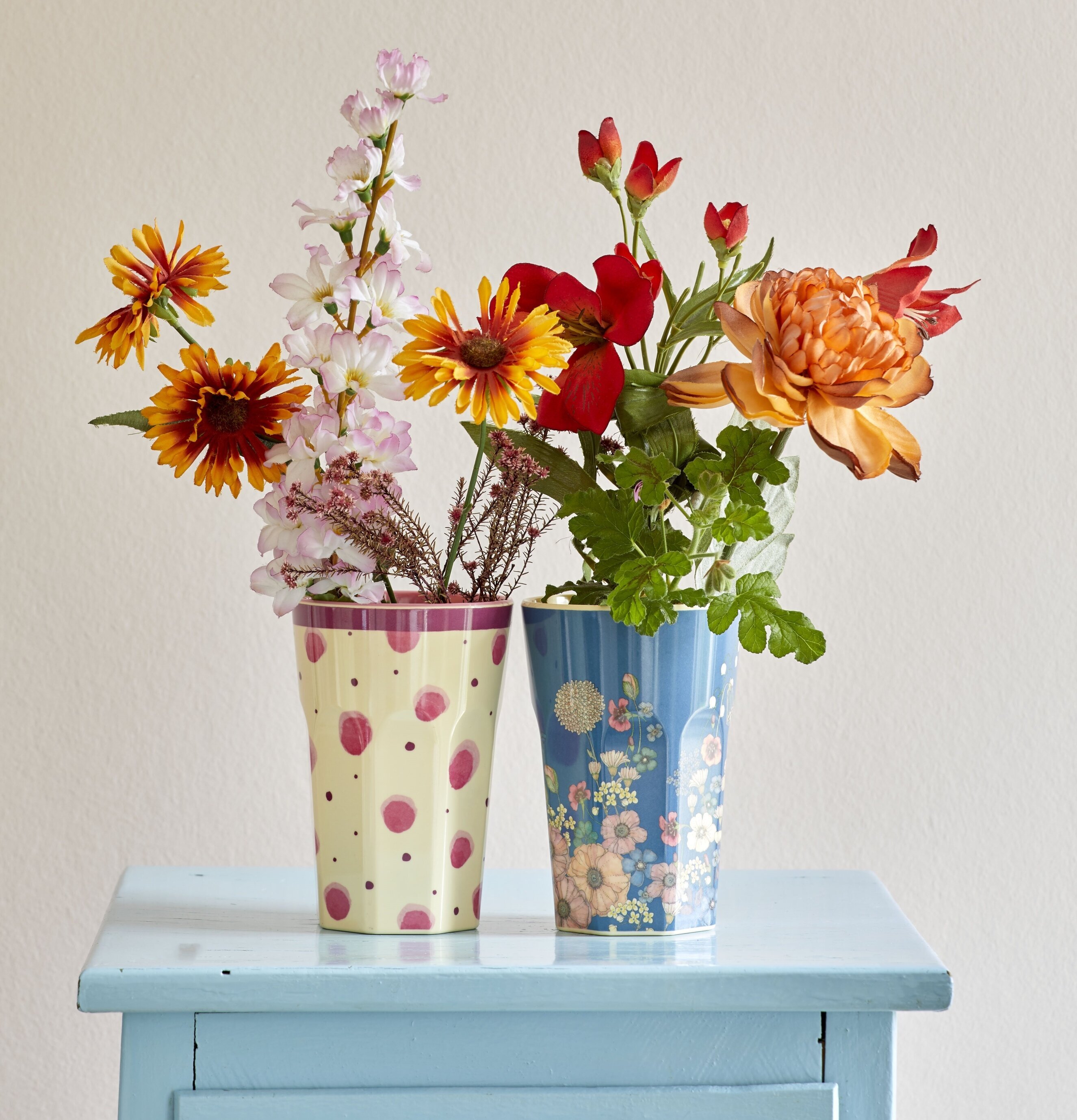 Bild av färgglada muggar och blommor på ljusblå byrå