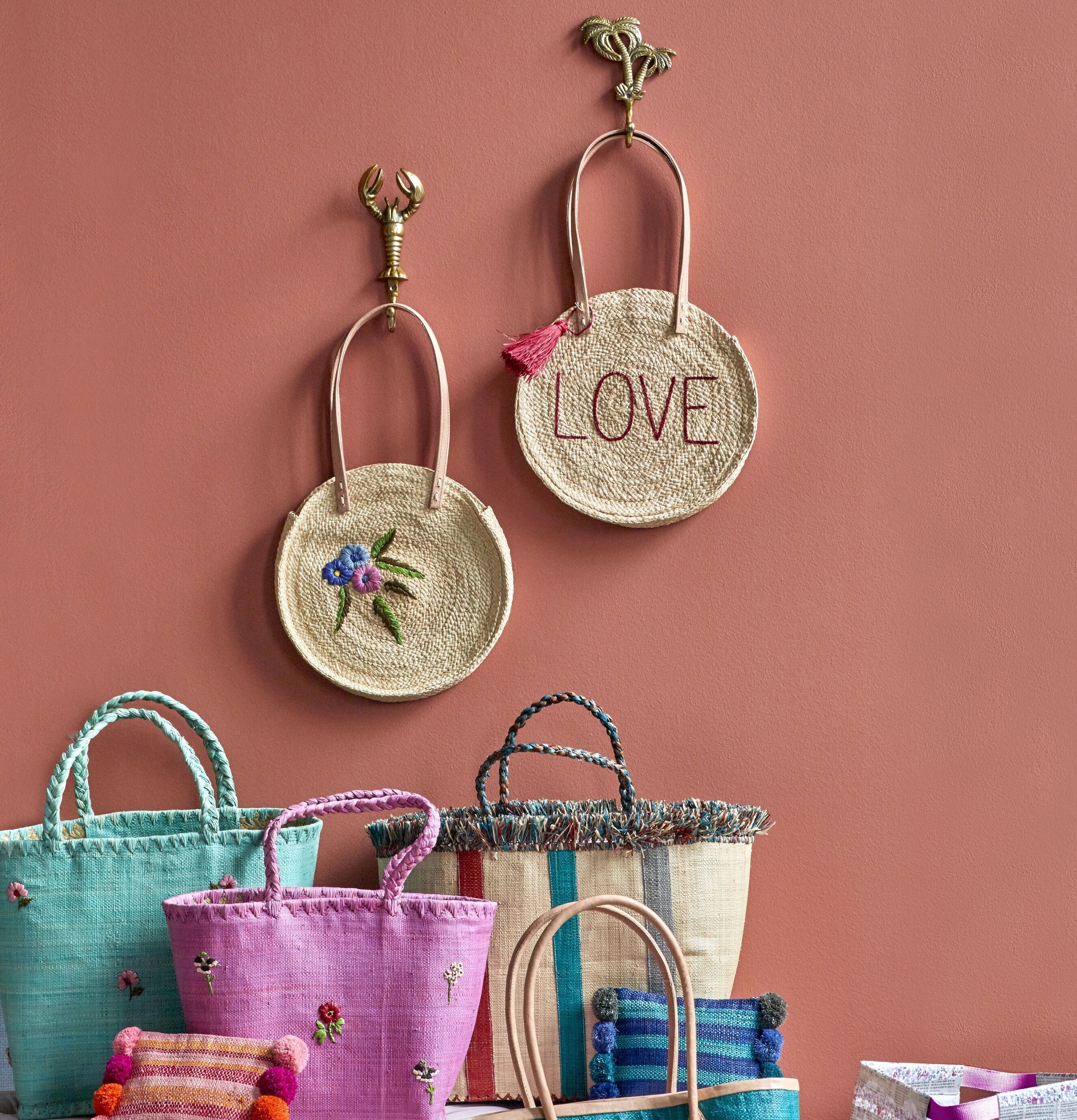 Väska Raffia Love från Rice hängandes på roströd vägg