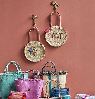Väska Raffia Love från Rice hängandes på roströd vägg