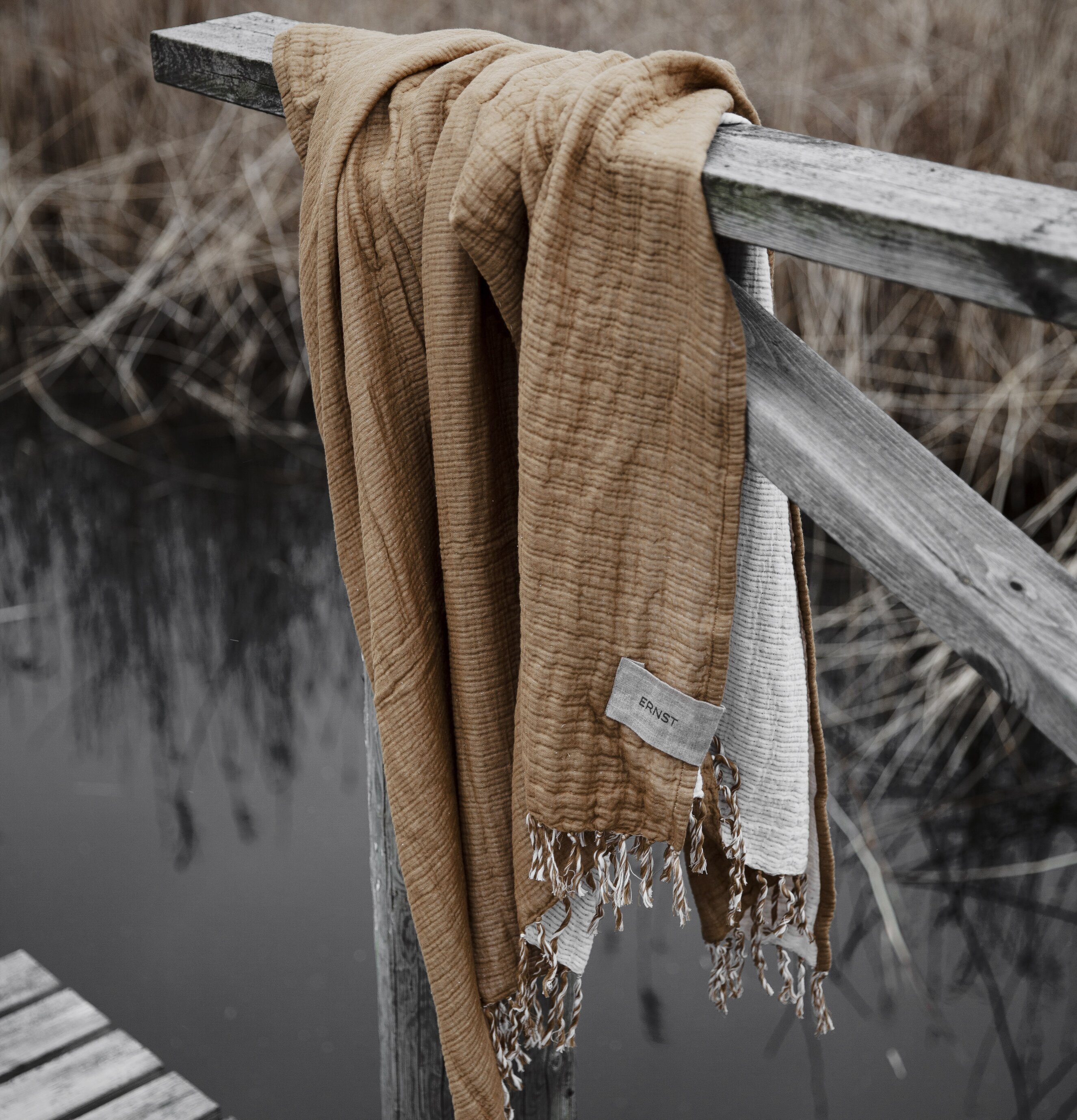 Bomullspläd Saffran från Ernst draperad över trägrind vid sjö