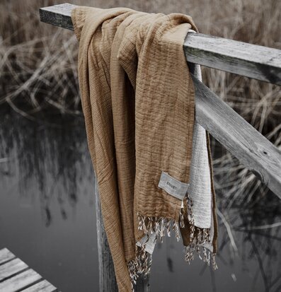 Bomullspläd Saffran från Ernst draperad över trägrind vid sjö