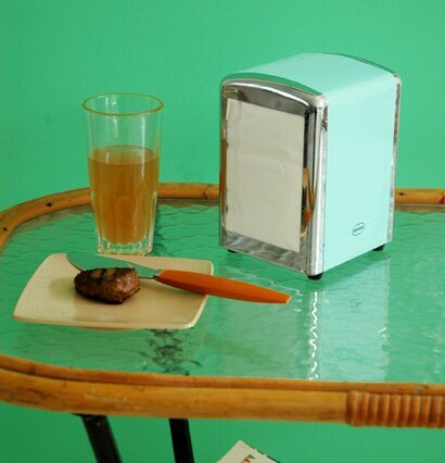 Servettställ Aqua från Cabanaz på glasbord med dryck och kaka