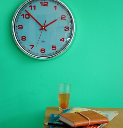 Väggklocka Aqua från Cabanaz på grön vägg med träbord