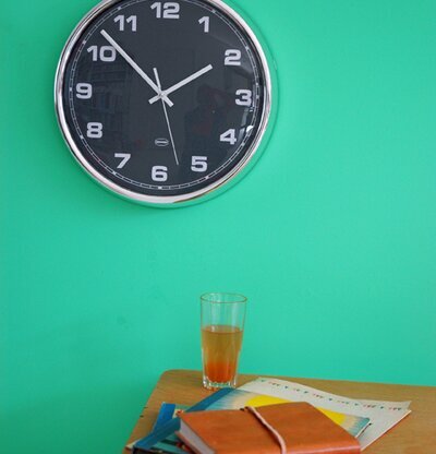 Väggklocka Grå från Cabanaz på grön vägg ovanför träbord