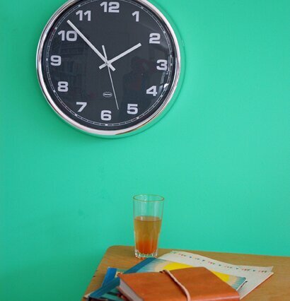 Väggklocka Grå från Cabanaz på grön vägg ovanför träbord