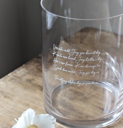 Bild av elegant glasvas med graverad text och blomma