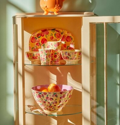 Assiett Peach Print från Rice i ett vitrinskåp med solstrålar