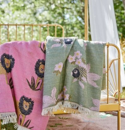 Pläd Goldfish Sage Green från Rice hänger över guldsäng