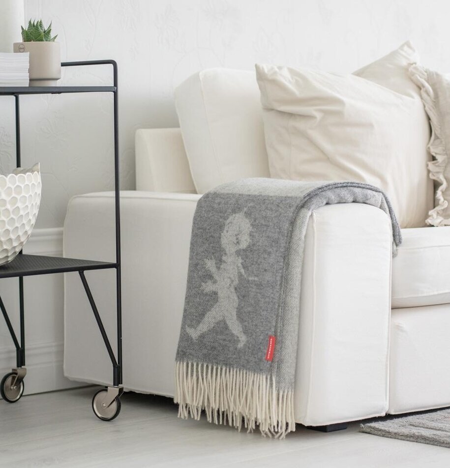 Pläd Ljusgrå Solstickan från Solstickan på en krämvit soffa