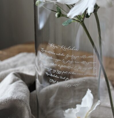 Bild av elegant glasvas med vit blomma och inskription