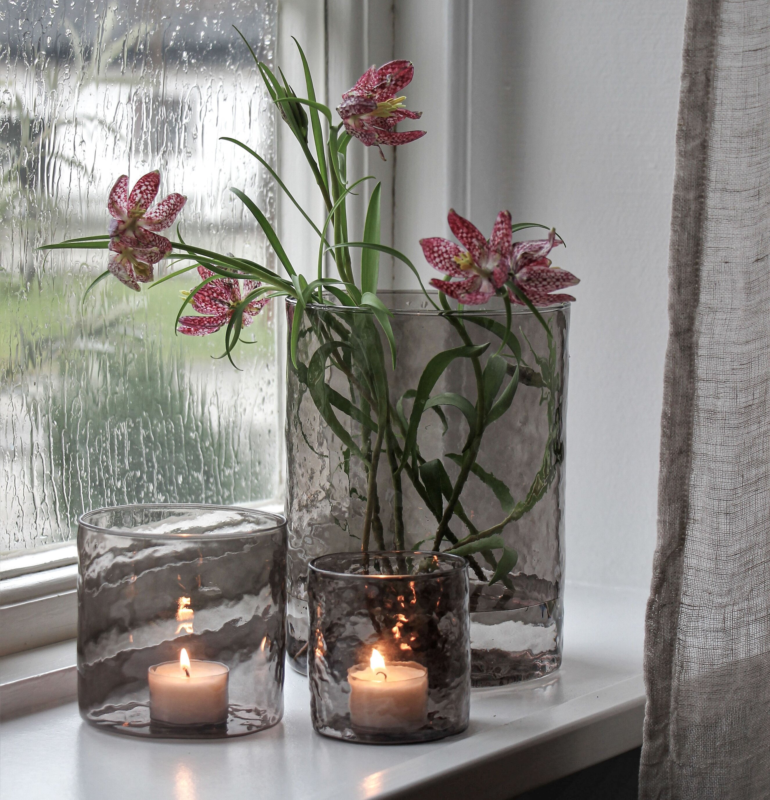 Bild av stilrena ljuslyktor i regnvåt fönsternisch