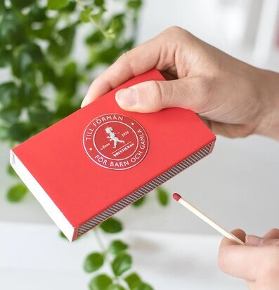 Tändsticksask Röd från Solstickan i en hand med grön växt