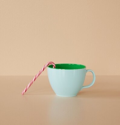 Foto av färgglad mugg med polkagris på neutral bakgrund