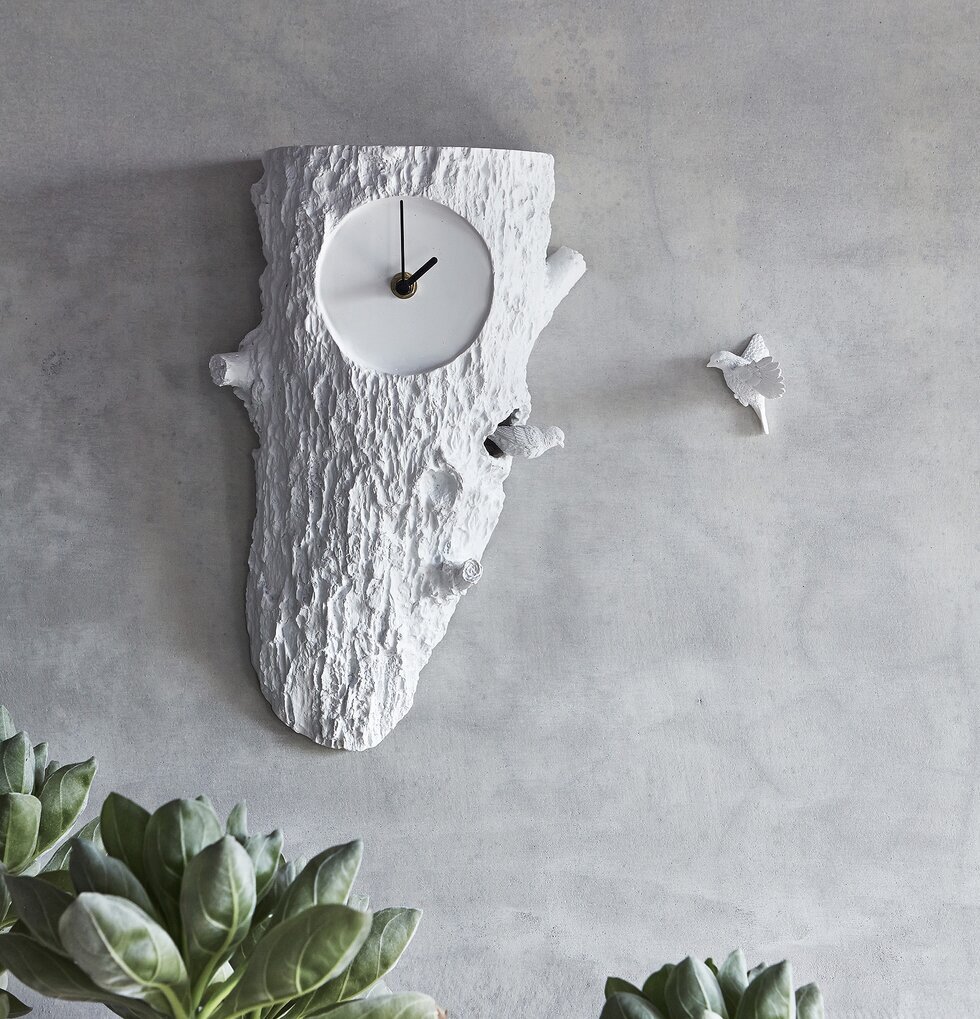 Väggklocka Cuckoo - Haoshi Design mot grå vägg med växter