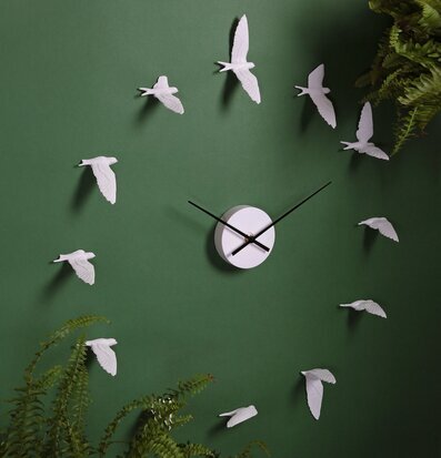 Väggklocka Swallow - Haoshi Design på grön vägg med växter