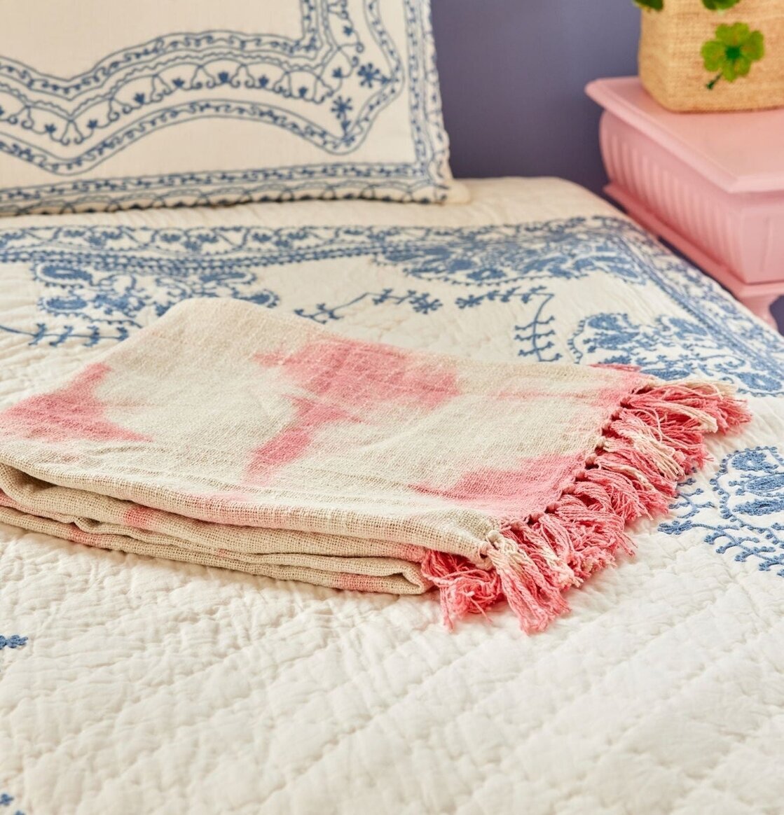 Bomullsfilt Batik Rosa från Rice på en säng med blått täcke