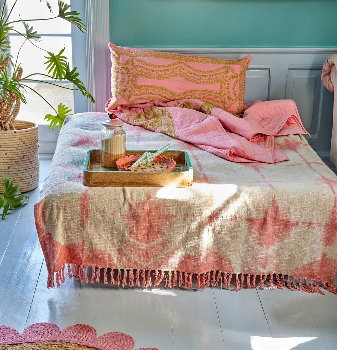 Bomullsfilt Batik Rosa från Rice på en säng i ett ljust rum