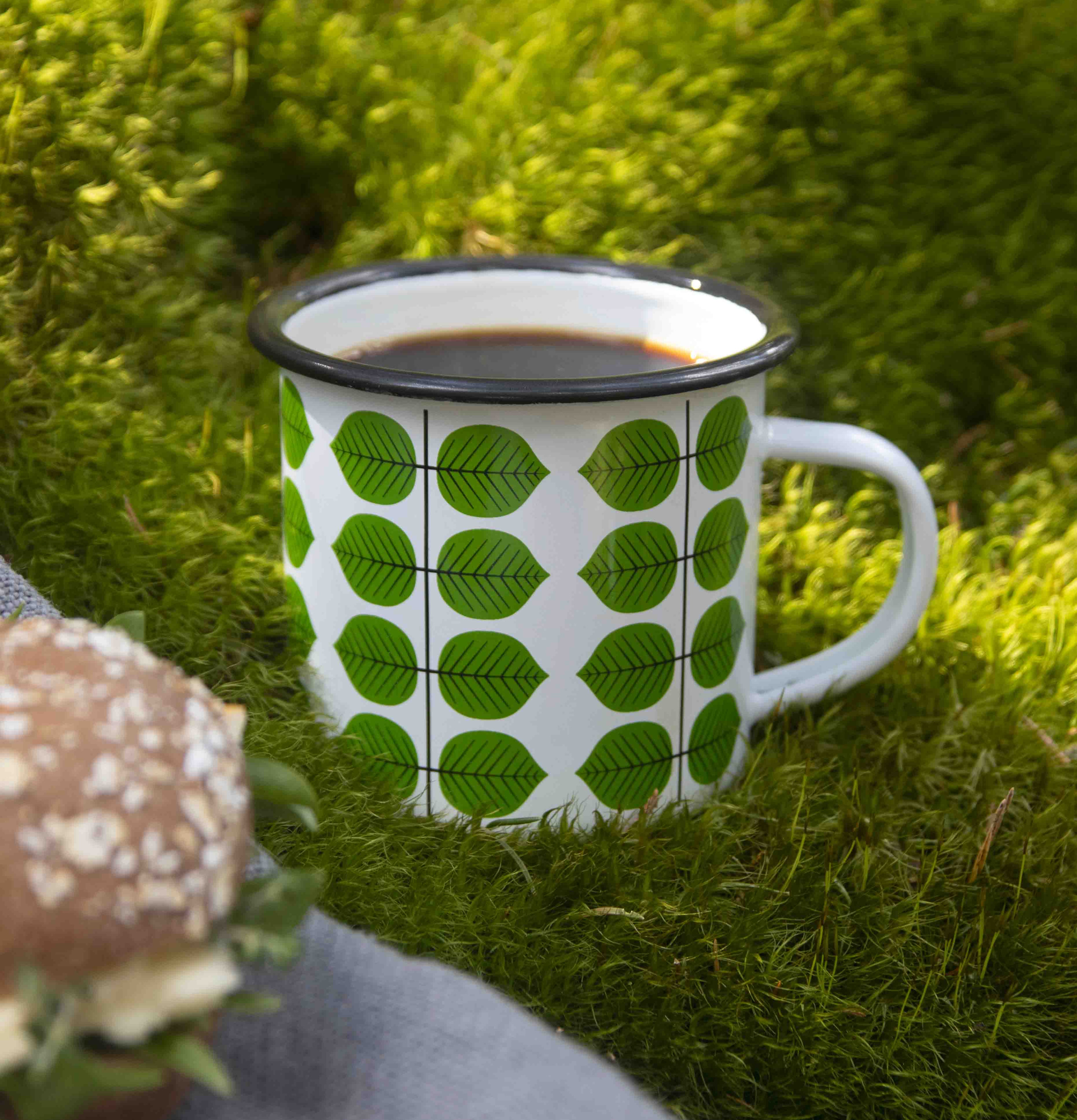 Foto av emaljmugg i naturskön miljö med smörgås