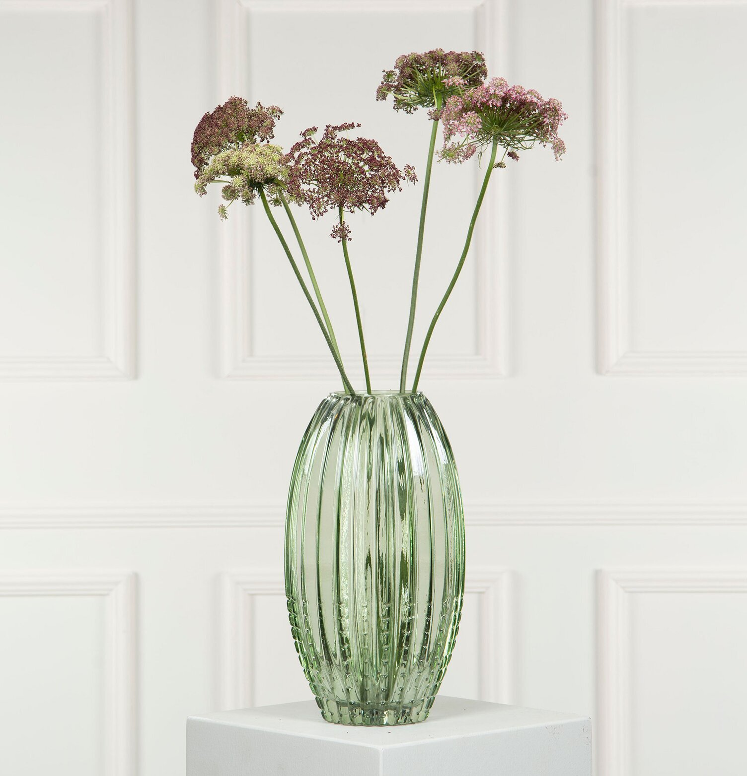 Bild av grön vas med blommor på podium i harmonisk stil