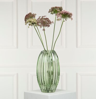 Bild av grön vas med blommor på podium i harmonisk stil