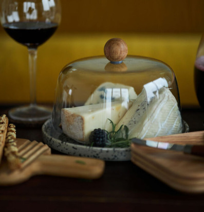 Foto av elegant ostkupa med träknopp och vin i bakgrunden
