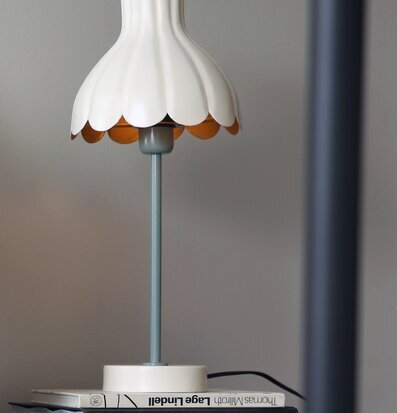 Bild av bordslampa på hylla med böcker och grå vägg