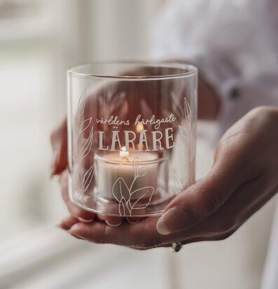 Bild på glaslykta med text och floralt motiv i varma toner