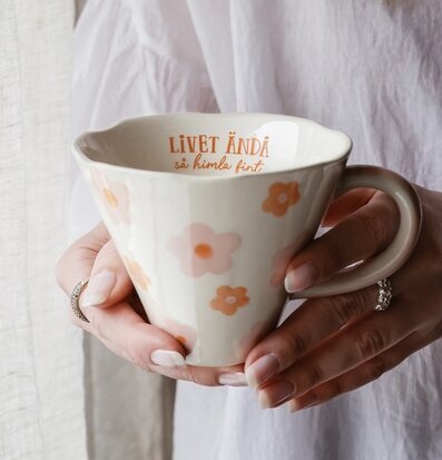 Bild av handmålad mugg med blommor och varm text i närbild