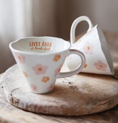 Bild av två keramikmuggar med blommor på rustik träbricka