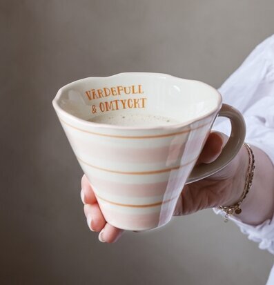 Bild på hand som håller pastellmugg med vågig kant och text