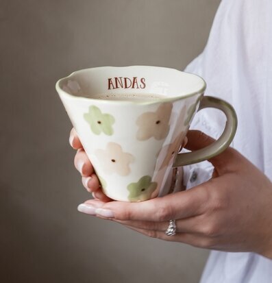 Bild på hand som håller blomstrande mugg med texten Andas