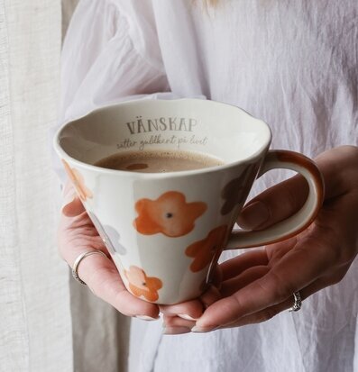 Bild av handhållen kopp med blommor och varm dryck i hemmet