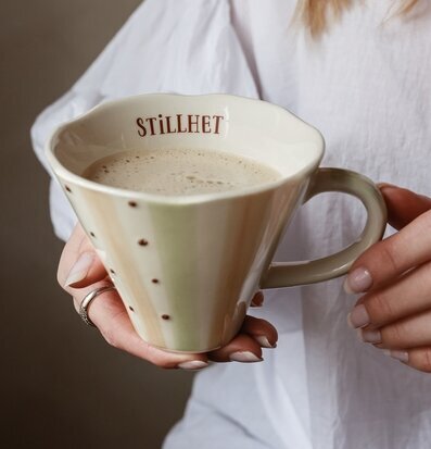 Bild på hand som håller keramikkopp med kaffe i mjukt ljus