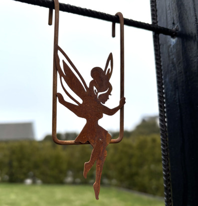 Bild på dekorativ älva i rostig metall på gunga i trädgård