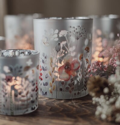 Bild med ljuslyktor och blommor i mjukt ljus på träbord