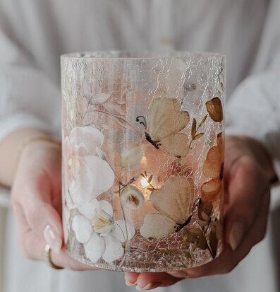 Bild på ljuslykta med blommor och fjärilar i mjuka färger