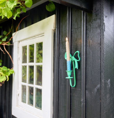 Bild av svart träfasad med färgglad ljusstake och grönska