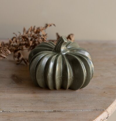 Bild av grön keramikpumpa på ljust träbord i höstig miljö