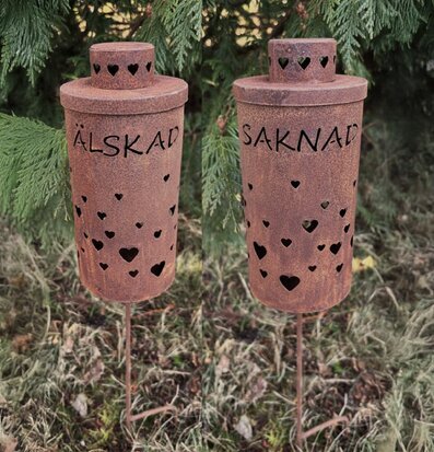 Bild av gravlykta med hjärtan och text i rofylld naturmiljö