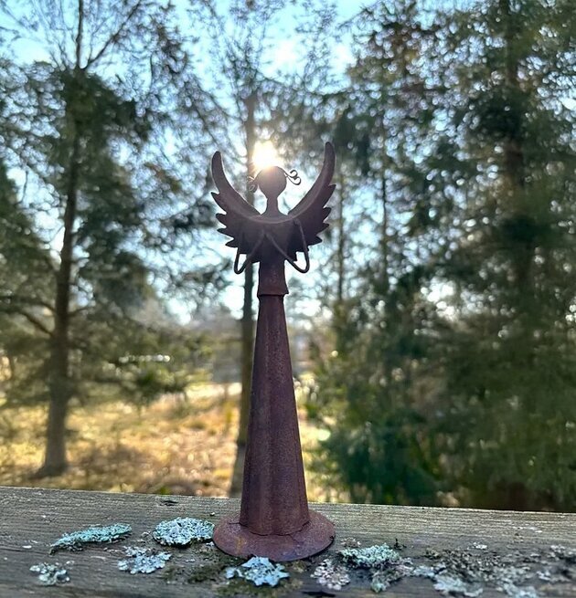 Bild av rostig ängelfigur i metall på trä med skogsbakgrund